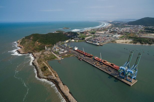 Vista aérea do Porto de Imbituba, em Santa Catarina, com navios, docas, guindastes e a costa brasileira.