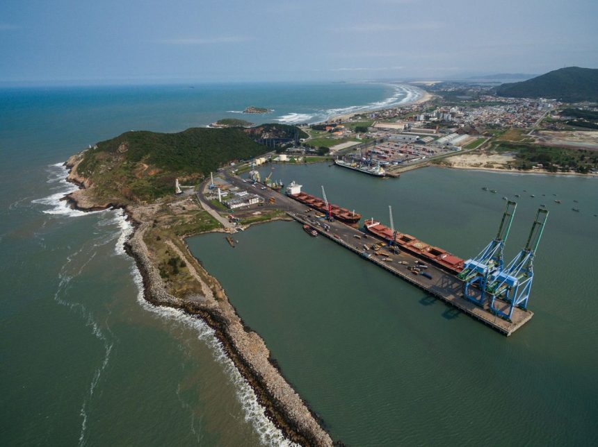 Vista aérea do Porto de Imbituba, em Santa Catarina, com navios, docas, guindastes e a costa brasileira.